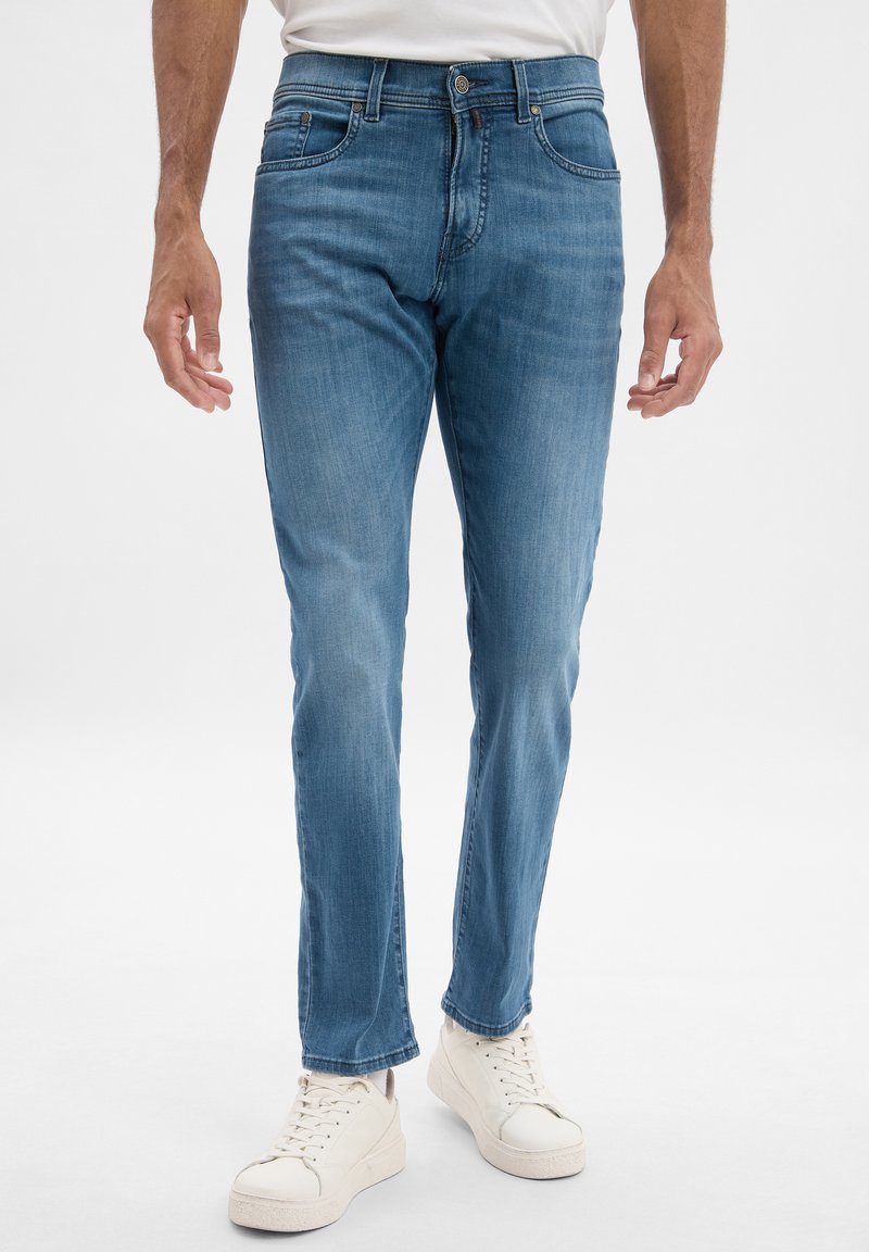 Jeans en denim bleu clair avec une coupe droite, design à cinq poches, légères décolorations et détails cousus. Associés à des baskets blanches.