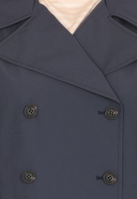 Cappotto doppiopetto blu navy con grandi bottoni neri, ampio colletto e superficie liscia. Cuciture dettagliate lungo i bordi.