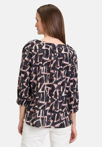 Blusa nera e rosa a fantasia con vestibilità ampia, maniche a tre quarti e scollo rotondo. Tessuto leggero e testurizzato con piega sul retro.