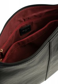 Interno di una borsa a mano in pelle nera testurizzata con una fodera in tessuto rosso scuro. Dotata di due scomparti con cerniera e una piccola etichetta nera.