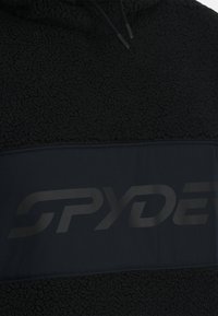 Pullover in pile nero con una finitura testurizzata e una fascia nera uniforme che presenta un grande logo Spyder in una finitura opaca sottile.