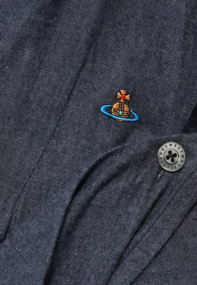 Tela gris oscuro con un logo de orbe y cruz bordado en azul, junto a un botón negro con texto blanco.