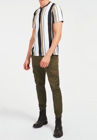 Camiseta de rayas en blanco, negro y verde oliva, con cuello redondo. Combinada con pantalones cargo verde oliva y botas negras con cordones.