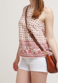 Hihaton, kreemi tank-top punaste lillemusteriga allääres. Kombineeritud valgete lühikesed püksid ja pruuni õlarihmaga kott.