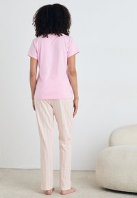 T-shirt de algodão rosa claro combinada com calças de pijama listradas em tons pastel. As calças apresentam riscas verticais em cores suaves.