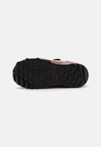 Semelle en caoutchouc noire avec des crans profonds, attachée à un dessus rose clair en textile avec une sangle noire.