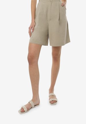 Shorts beige en tissu léger, avec une taille haute, des plis et une coupe décontractée. Associés à des sandales à glissière de couleur claire.