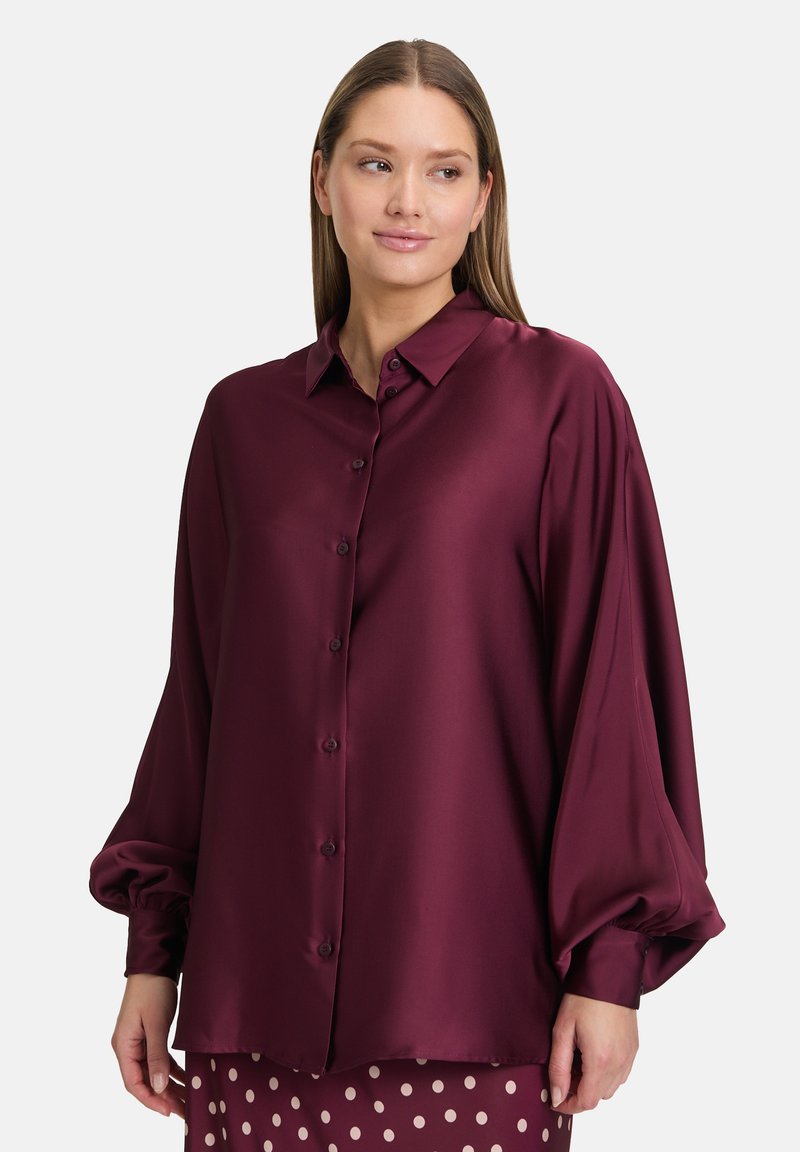 Burgundy satin blouse with a relaxed fit, long puff sleeves, a button-up front, and a classic collar. Smooth texture and elegant drape.