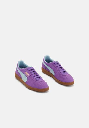 Paire de baskets Puma en daim violet avec des bandes bleu clair et des semelles en caoutchouc marron sur fond blanc.