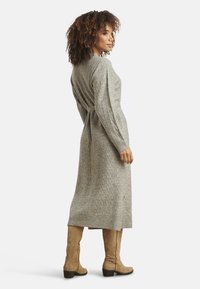 Vestito grigio lavorato a maglia con motivo a rilievo, caratterizzato da maniche lunghe e un fiocco sul retro. Indossato con stivali beige alti fino al ginocchio.