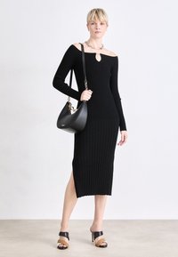 Black ribbed knit dress with off-shoulder neckline and keyhole detail. Includes side slit, paired with a black handbag and heeled sandals.