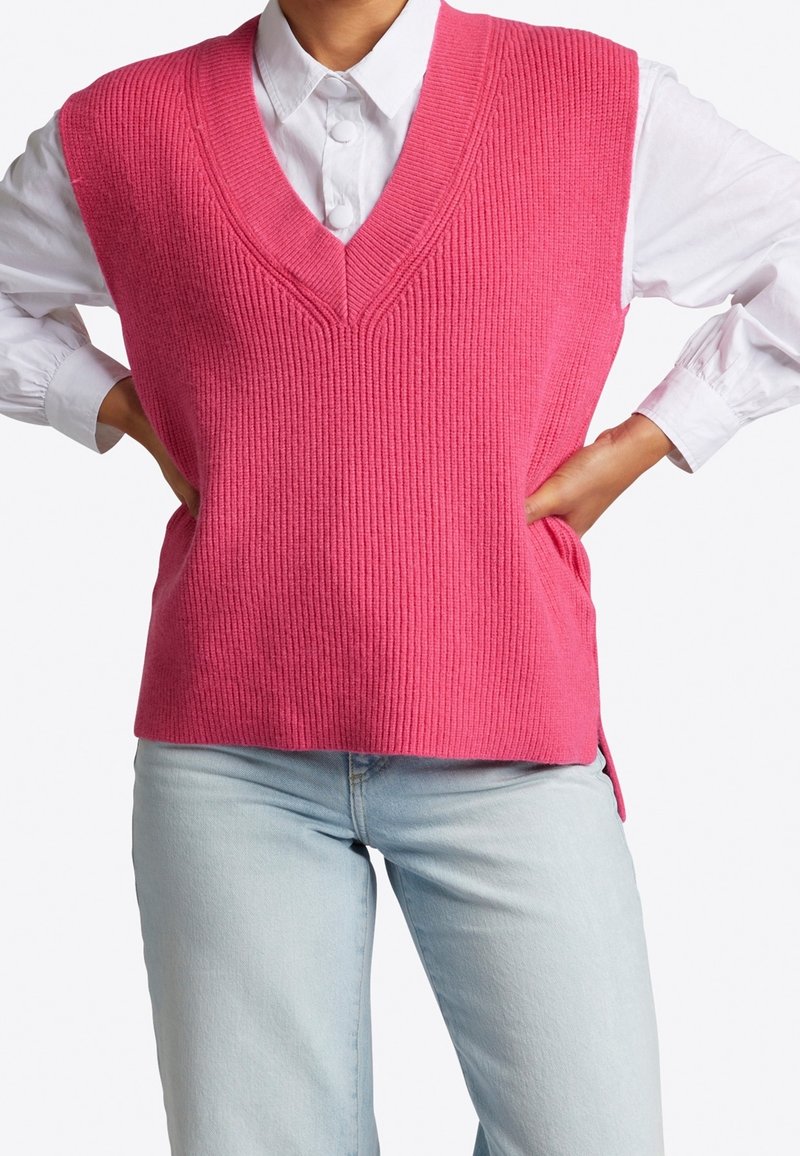 Helles pinkes Strickwesten mit V-Ausschnitt und geripptem Muster, über einem weißen Hemd mit Knopfleiste getragen. Sauberes, lässiges Design mit seitlichen Schlitzen.