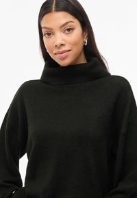 Sweater de gola alta preto com um corte descontraído, textura suave e mangas largas. Apresenta uma gola alta e dobrada para maior conforto.