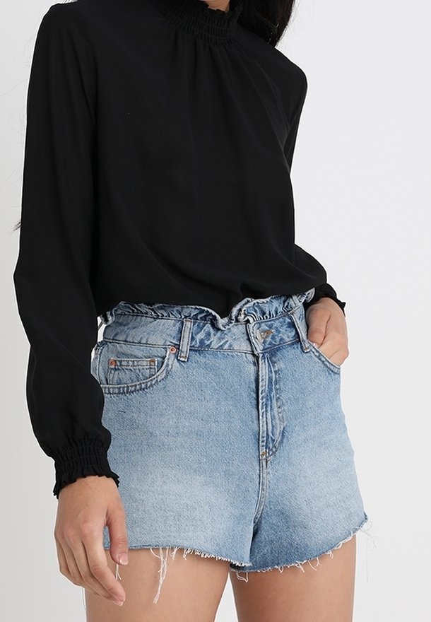 Haut noir à manches longues avec un col haut froncé, associé à un short en denim bleu clair avec un ourlet effiloché et une taille élastique.