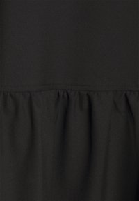 Black fabric with a smooth upper section and a gathered, ruffled lower section separated by a horizontal seam.