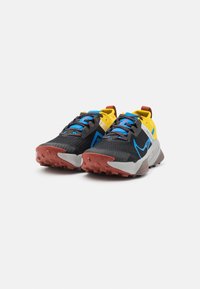 Chaussures de trail avec une tige en mesh noire, des accents jaunes, des lacets bleus et une semelle extérieure rouge pour la traction. Comprend un logo et des éléments réfléchissants.