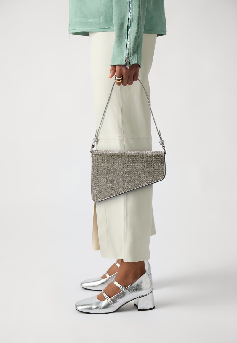 Borsa a pochette argento con design diagonale, superficie texturizzata e sottile tracolla in metallo, abbinata a scarpe con tacco a blocco metallico lucido.