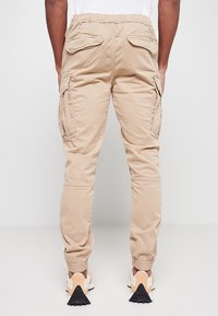 Pantalons cargo beiges avec une taille élastique, plusieurs poches latérales et des poignets côtelés. Fabriqués en tissu léger, avec une coupe décontractée.