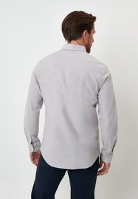 Camisa gris claro de manga larga con cuello abotonado y botones en los puños, que presenta una textura sutil y un dobladillo redondeado.