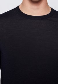 Svart stickad tröja med rund halsringning, med en slät textur och minimalistisk design. Tyget verkar lätt och åtsittande.