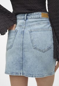 Blå denimkjol med lätt tvätt, medelhög midja och två bakfickor. Har en brun läderlapp på bakre midjebandet.