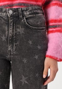 Mustat farkut, joissa on tähtikuvio, korkeavyötäröinen malli, etutaskut ja vetoketjullinen edessä. Yhdistetty vaaleanpunaiseen, raidalliseen neulepuseroon.