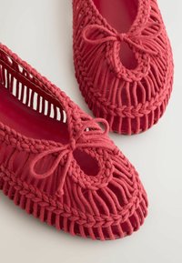Paire de chaussures plates en tissu tissé rouge avec des détails tressés et de petits nœuds à l’avant, exposées sur une surface blanche.