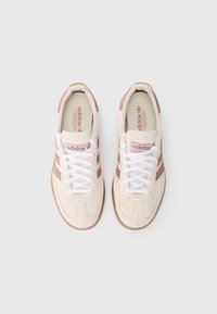 Béžové tenisky s ružovými pruhmi, bielymi šnúrkami a textúrovaným látkovým zvrškom. Podrážka je svetlohnedá gumená s logom Adidas na jazyku.