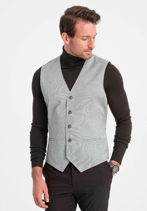 Grey patterned vest with a v-neck and five buttons, featuring two front pockets. Worn over a black turtleneck with a tailored fit.