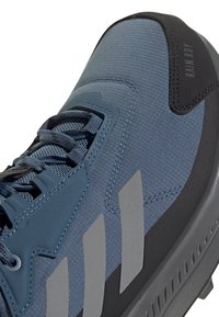 Zapatilla deportiva azul con parte superior texturizada, diseño de cordones y acentos grises. Presenta tres franjas grises audaces y una suela de goma gris.