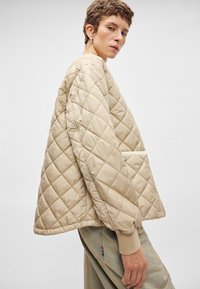 Κουβερτίνα μπεζ ζακέτα με χαλαρή εφαρμογή, featuring ριπ κολάρο και μανσέτες, και πλαϊνές τσέπες. Λείο υφή και μινιμαλιστικός σχεδιασμός.