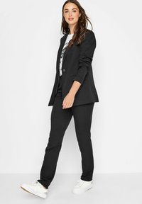Zwarte op maat gemaakte blazer en bijpassende broek, gecombineerd met een graphic t-shirt en witte sneakers. Glad materiaal, slim fit en klassiek ontwerp.