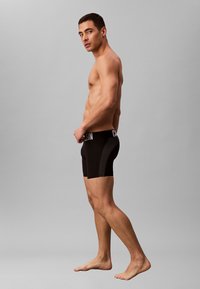 Calzoncillos bóxer negros con un panel texturizado en contraste, con una cintura prominente con logo. Tela suave, longitud hasta la mitad del muslo, diseño ajustado.