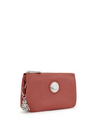 Cartera de nylon roja con un medallón y charm de logo plateado. Tiene un cierre de cremallera y una textura suave. Compacta y de forma rectangular.