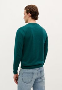 Teal, lange mouwen trui van zacht materiaal met een ronde hals en geribbelde boorden. Draag het met lichtblauwe jeans, wat een casual look weergeeft.
