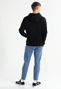 Black hoodie with a soft texture, featuring a hood and ribbed cuffs, paired with light blue jeans and black sneakers with white accents.