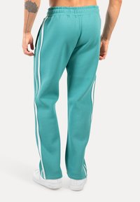 Pantalons de survêtement turquoise avec une coupe décontractée, dotés de bandes blanches sur les côtés et d'une taille élastique. Fabriqués en tissu doux et lisse.