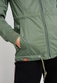 Zelená prošívaná bunda se zipovým uzávěrem, žebrovanými manžetami, bočními kapsami a nastavitelnou šňůrkou v dolním lemu. Obsahuje značenou visačku.