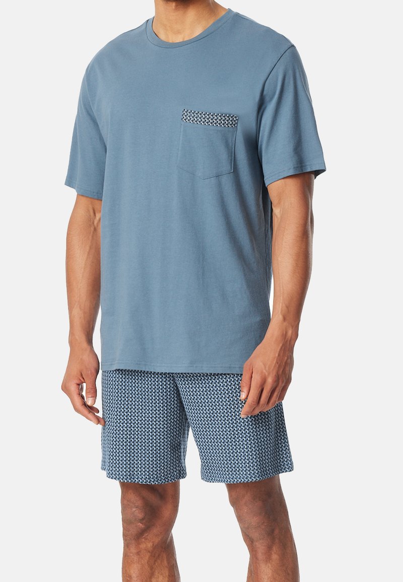 T-shirt in cotone blu con maniche corte e taschino sul petto a fantasia, abbinato a pantaloni corti blu con fantasia coordinata, caratterizzati da una vestibilità rilassata.