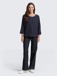 Navy blue oversized sweater with a round neckline and wide sleeves, paired with dark flared jeans and white sneakers. Smooth texture.