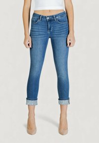 Kapeat siniset farkut, joissa on keskitason vyötärö, käännetyt lahkeet koristeellisella hopeisella yksityiskohdalla ja hienovarainen haalistuma jaloissa.