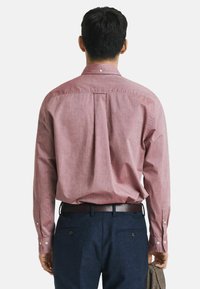 Rotes kariertes Hemd mit langen Ärmeln, Knopfmanschetten und Rückenpasse, kombiniert mit marineblauen Hosen und einem braunen Gürtel.