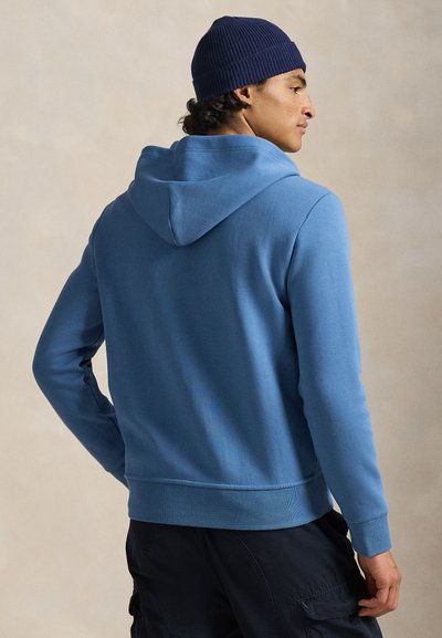 Μπλε φούτερ με κουκούλα από μαλακό ύφασμα, διαθέτει ρυθμιζόμενη κουκούλα με κορδόνια και μανσέτες με ριμπ ύφανση. Συνδυάζεται με σκούρο cargo παντελόνι, που έχει άνετη γραμμή.