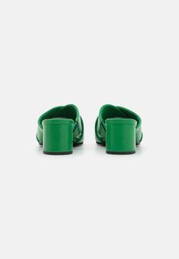 Chaussures en cuir vert à talons carrés avec un design à dos ouvert, présentant une texture lisse et une silhouette élégante, conçues pour un enfilage facile.