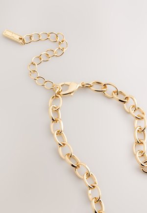 Collar de cadena de metal dorado con eslabones ovalados, equipado con un cierre de langosta y una pequeña cadena de extensión. Acabado con superficie lisa y brillante.