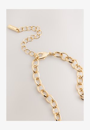 Kultainen metalliketju, jossa ovaalinmuotoiset lenkit, kiinnittyy hummeriklipsillä ja sisältää lyhyen jatkorenkaan. Pinta on sileä ja kiiltävä.