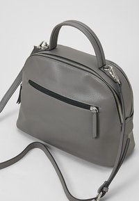 Harmaa nahkainen käsilaukku, jossa on kivetty pinta, ylhäällä olevat kahvat ja irrotettava olkahihna; sisältää edessä vetoketjupussin ja hopean väristä metalliosaa.