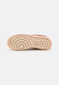 Sneaker sole with a textured cream color, featuring circular and wave patterns, and a logo at the center. Rubber material, durable design.