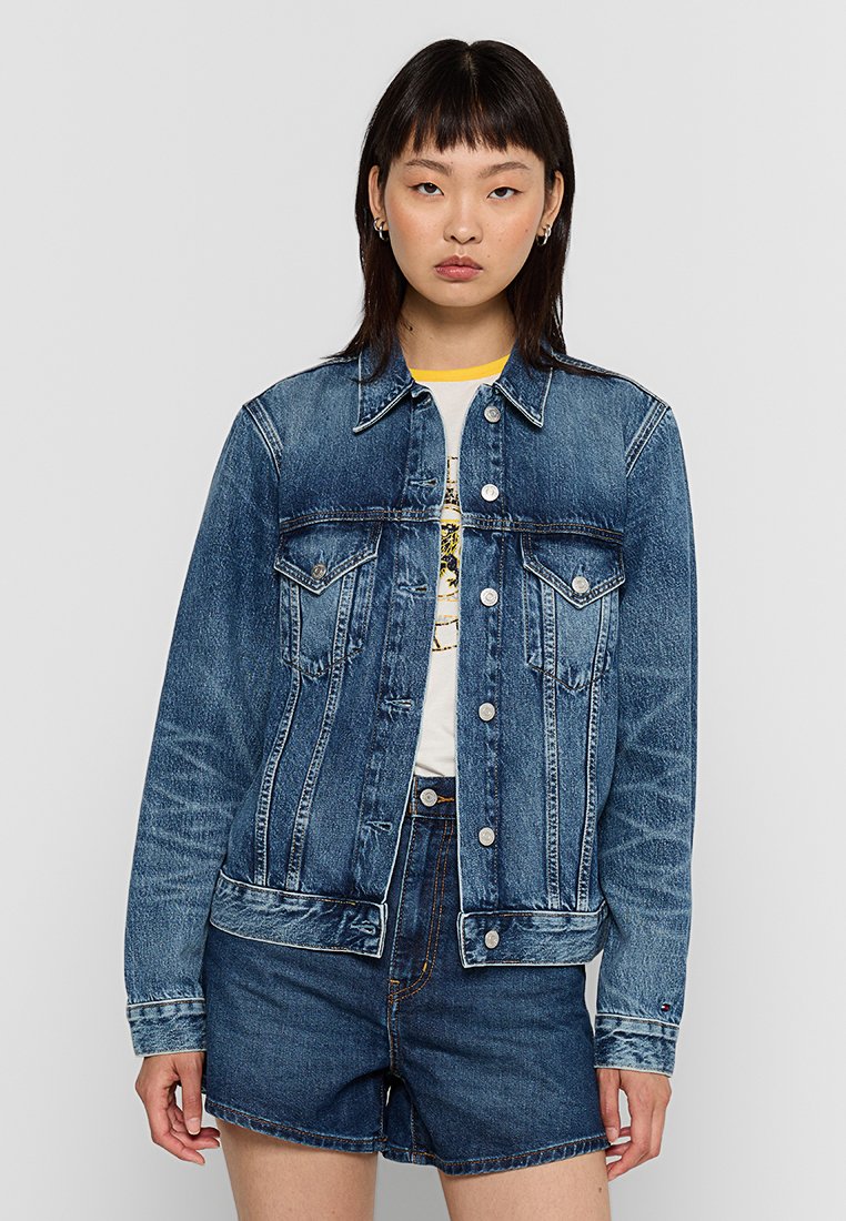 Blaue Jeansjacke mit klassischem Schnitt, spitzem Kragen, Knopfverschluss und zwei frontalen Taschen. Trägt man über einem weißen T-Shirt und Denim-Shorts.