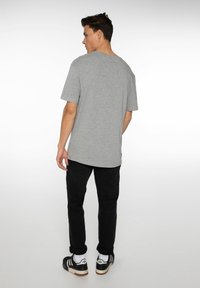 Grijze katoenen t-shirt met een relaxte pasvorm, brede ronde hals en korte mouwen, gecombineerd met zwarte broeken en sneakers.